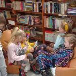 Grupa 6-latków w trakcie siedzenia na pufach i stania słucha dziewczynki jak czyta bajkę